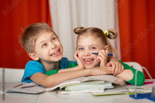 cute cheerful children of 8-9 years old, schoolchildren did homework at the table, a lot of textbooks are on the desk, children are happy looking at the camera in an embrace