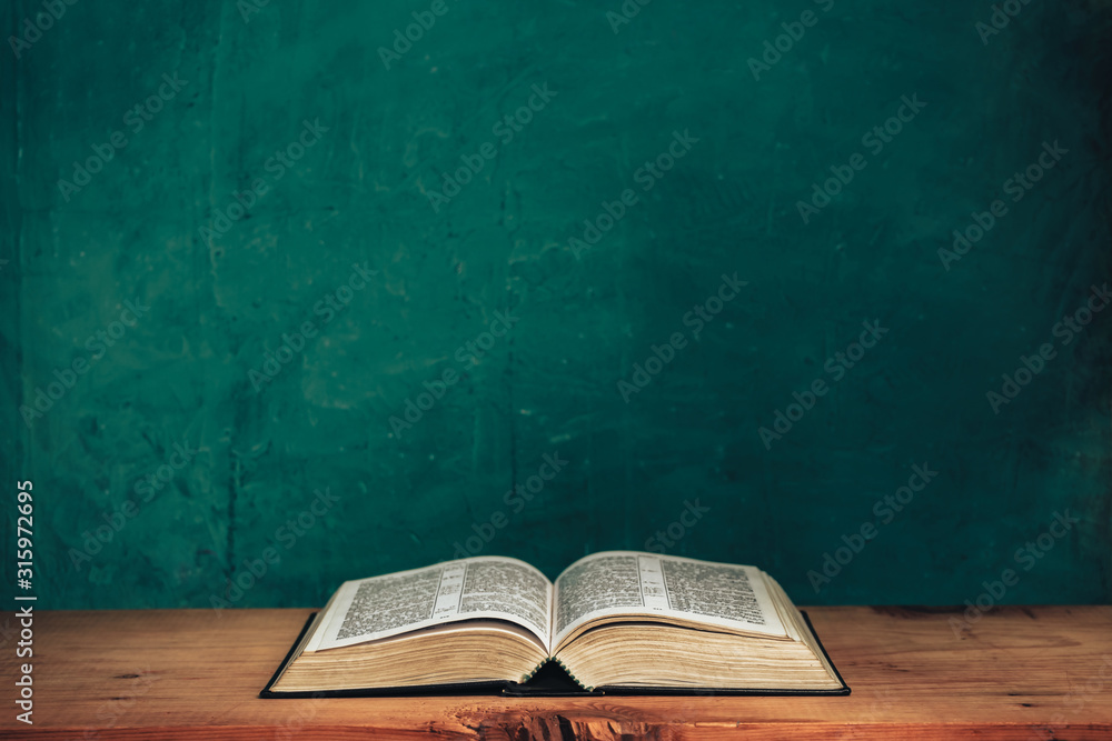 Fototapeta Open bible on a red old wooden table. Beautiful green wall background.