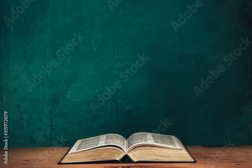 Open bible on a red old wooden table. Beautiful green wall background.