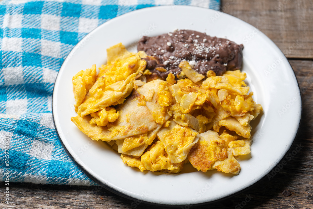 Mexican scrambled eggs with corn tortilla also called migas on wooden background