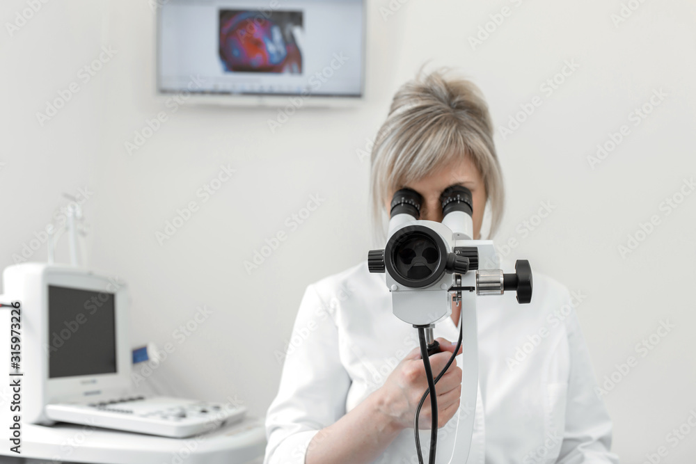 Fototapeta premium Female blond doctor gynecologist looks through a colposcope. Examination by a gynecologist. Female health concept