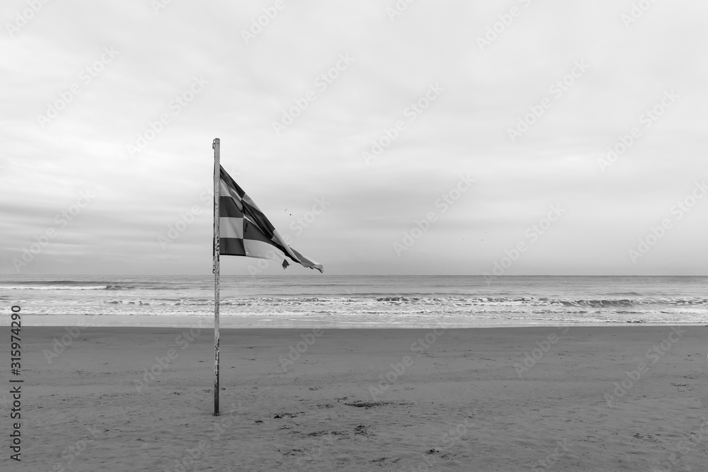 Waving old flag on the empty beach. Black and white photo - obrazy, fototapety, plakaty 