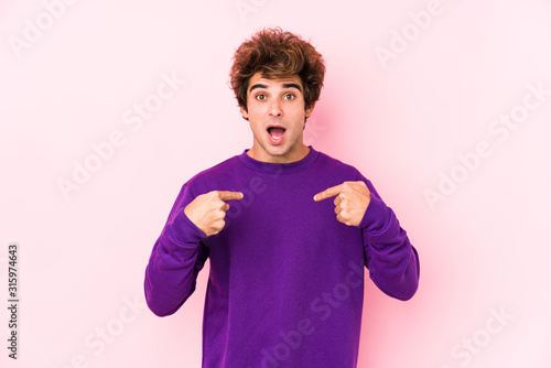 Young caucasian man against a pink background isolated surprised pointing with finger, smiling broadly.