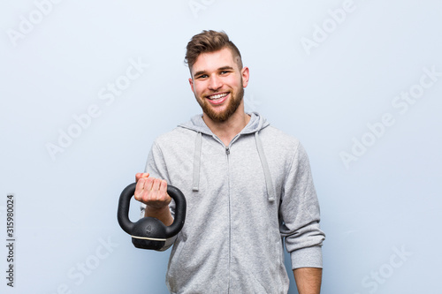 Young caucasian sportsman holding a dumbbell happy, smiling and cheerful.