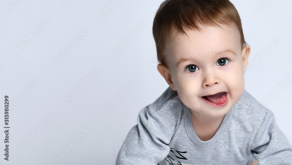Portrait of little baby boy toddler in grey casual jumpsuit lying on floor, looking at camera and smiling over white background Portrait of little baby boy toddler in grey casual jumpsuit lying on floor, looking at camera and smiling over white background