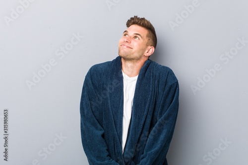 Young caucasian man wearing pajama dreaming of achieving goals and purposes