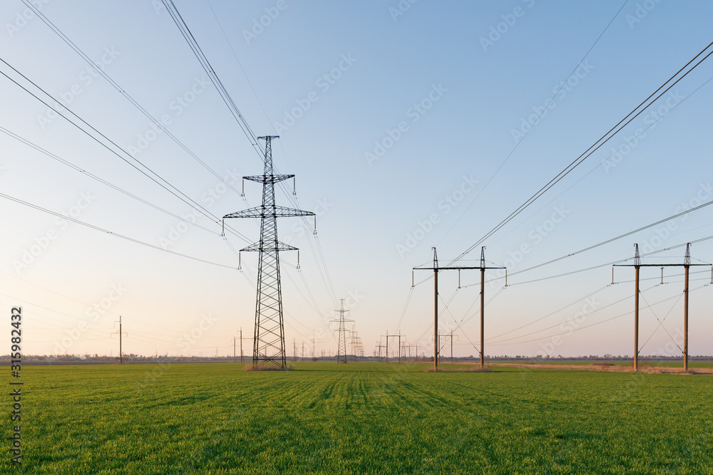 Electrical net of poles on a panorama of blue sky and green meadow