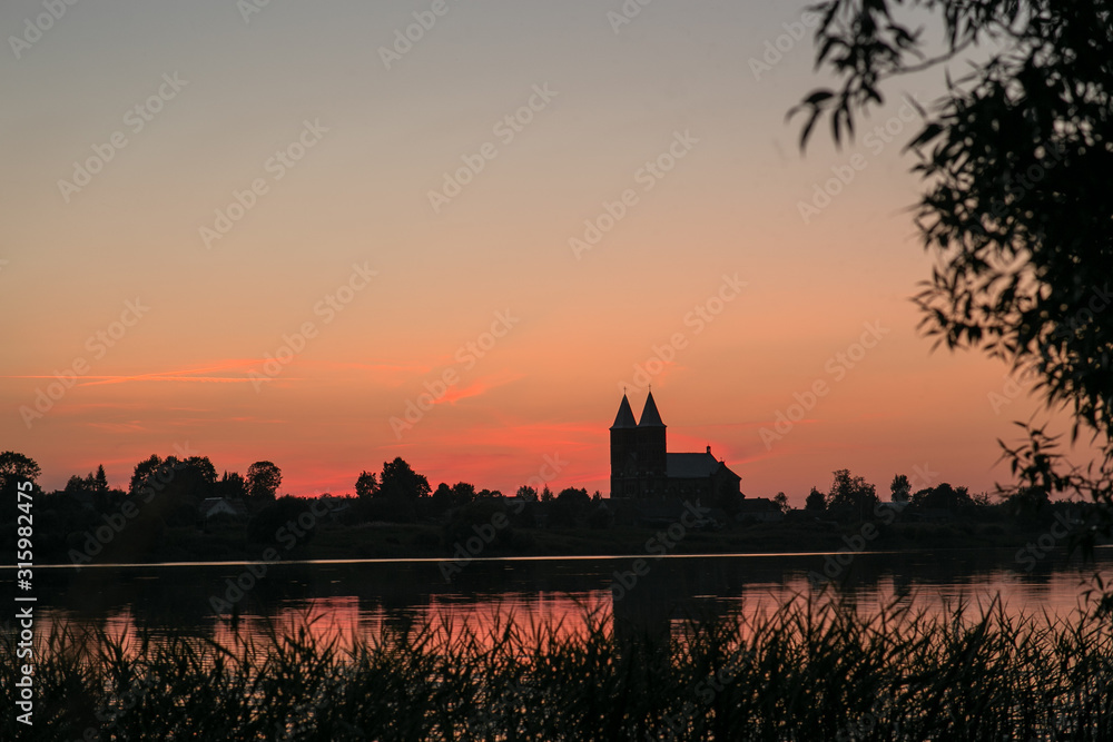 Two towers of the temple on a background of red, sunset sky. In the foreground is a reflection in the lake.