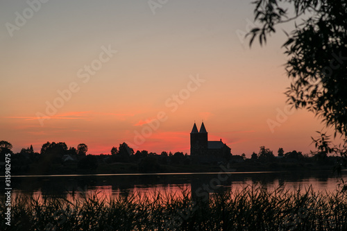 Two towers of the temple on a background of red, sunset sky. In the foreground is a reflection in the lake.