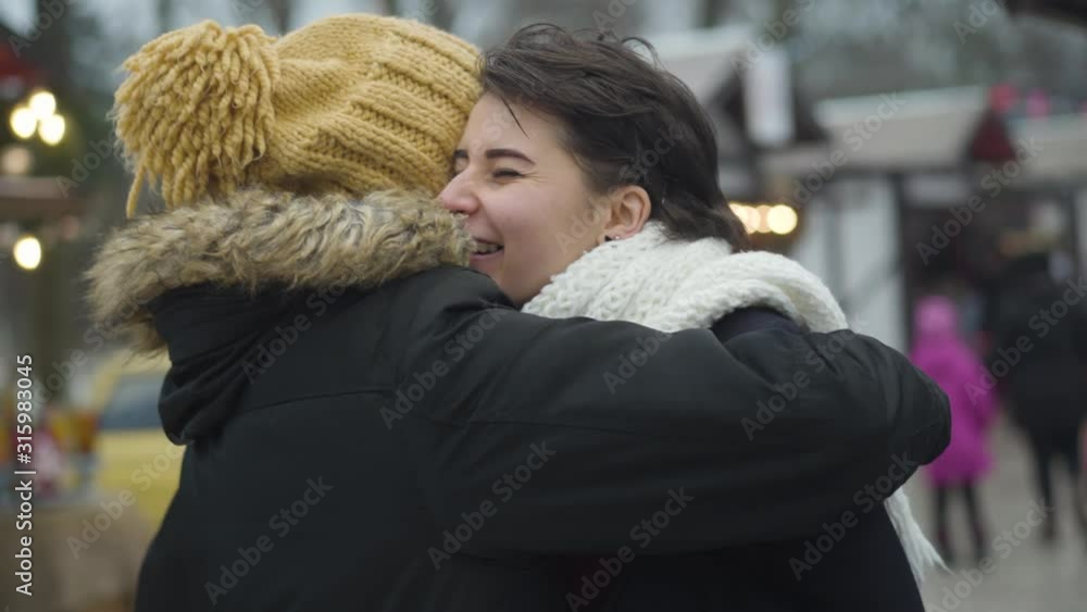 Young Caucasian man running up from the background to his girlfriend holding coffee cups. Happy beautiful woman hugging her boyfriend. Cheerful couple warming up with hot drink outdoors. Love, dating. Young Caucasian man running up from the background to his girlfriend holding coffee cups. Happy beautiful woman hugging her boyfriend. Cheerful couple warming up with hot drink outdoors. Love, dating.