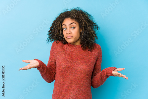 Young african american curly hair woman doubting and shrugging shoulders in questioning gesture. photo