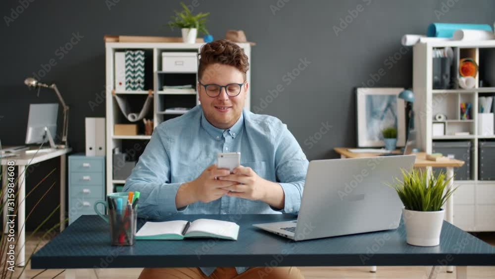 Handsome young man using smartphone in office at desk smiling having fun enjoying communication online. Modern technoology and millennials concept. Handsome young man using smartphone in office at desk smiling having fun enjoying communication online. Modern technoology and millennials concept.