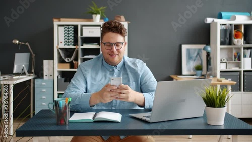 Handsome young man using smartphone in office at desk smiling having fun enjoying communication online. Modern technoology and millennials concept. photo