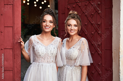 Obraz na płótnie Beautiful retro styled bridesmaids ladies in gorgeous elegant stylish light grey silver floor length dresses in old beautiful European city welcome greeting guests at the gate. w salonie