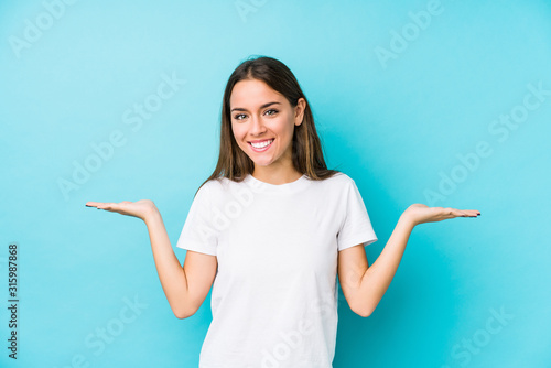 Young caucasian woman  isolated makes scale with arms, feels happy and confident.