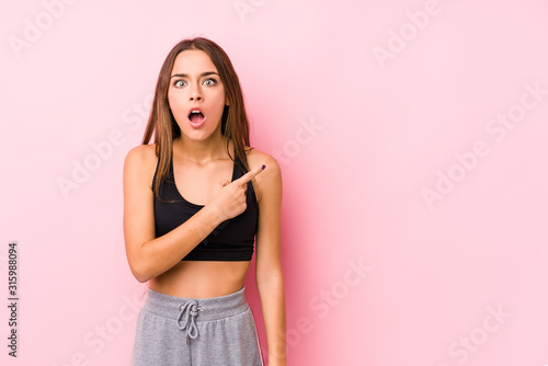 Young caucasian fitness woman posing in a pink background pointing to the side