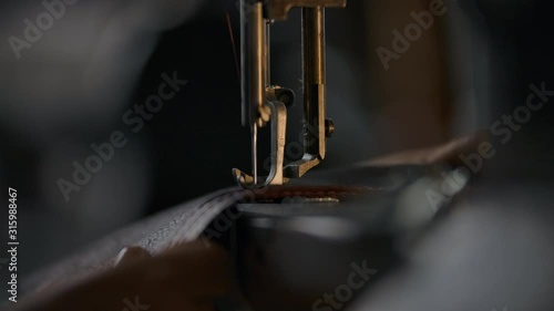Close-up view of working sewing machine presser foot, stitching in slowmotion. Tailor's hand holding sewing leather carefully. Manufacturing handicraft unique individual bags, belts, accessories 