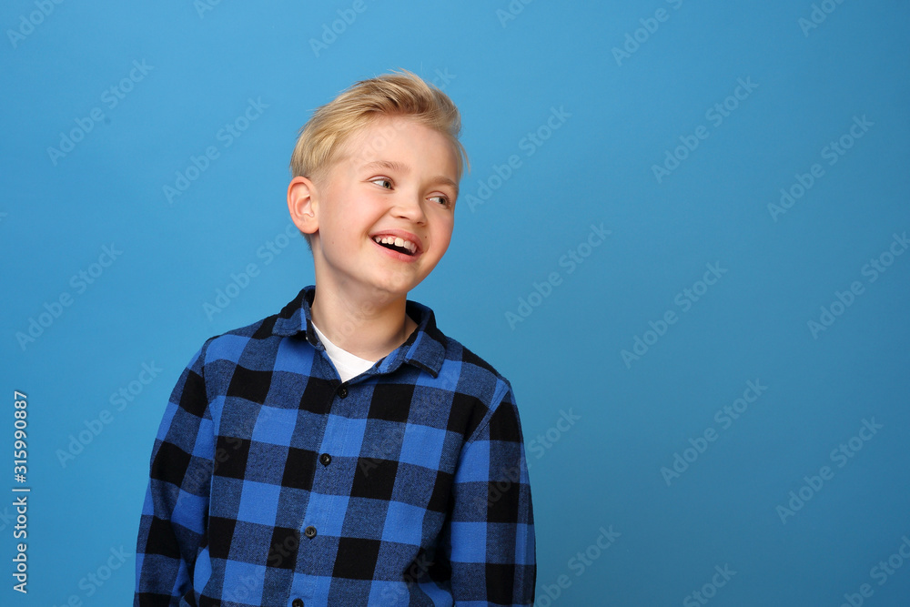 Smiling boy, happy child.  Happy, smiling boy on a blue background expresses emotions through gestures. - obrazy, fototapety, plakaty 