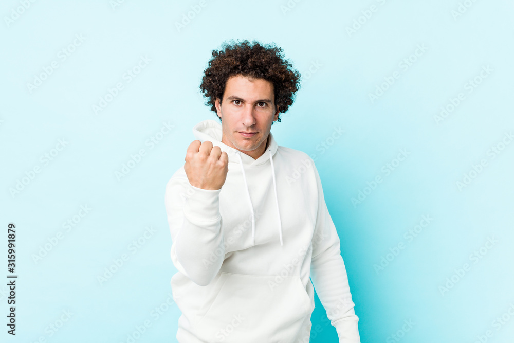Young sporty man against a blue background showing fist to camera, aggressive facial expression. Young sporty man against a blue background showing fist to camera, aggressive facial expression.