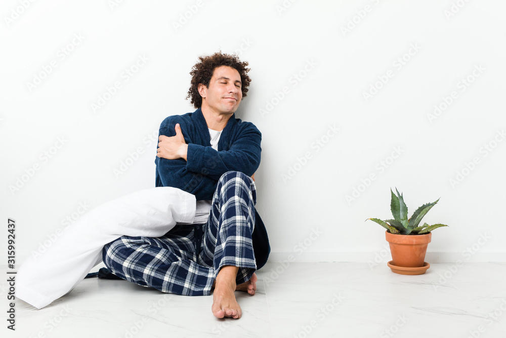 Mature man wearing pajama sitting on house floor hugs, smiling carefree and happy. Mature man wearing pajama sitting on house floor hugs, smiling carefree and happy.