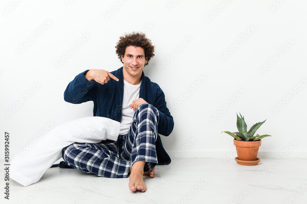 Mature man wearing pajama sitting on house floor person pointing by hand to a shirt copy space, proud and confident Mature man wearing pajama sitting on house floor person pointing by hand to a shirt copy space, proud and confident