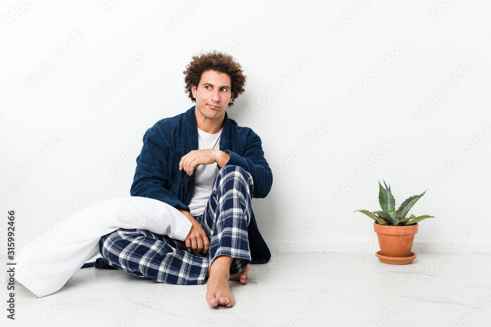 Mature man wearing pajama sitting on house floor confused, feels doubtful and unsure. Mature man wearing pajama sitting on house floor confused, feels doubtful and unsure.