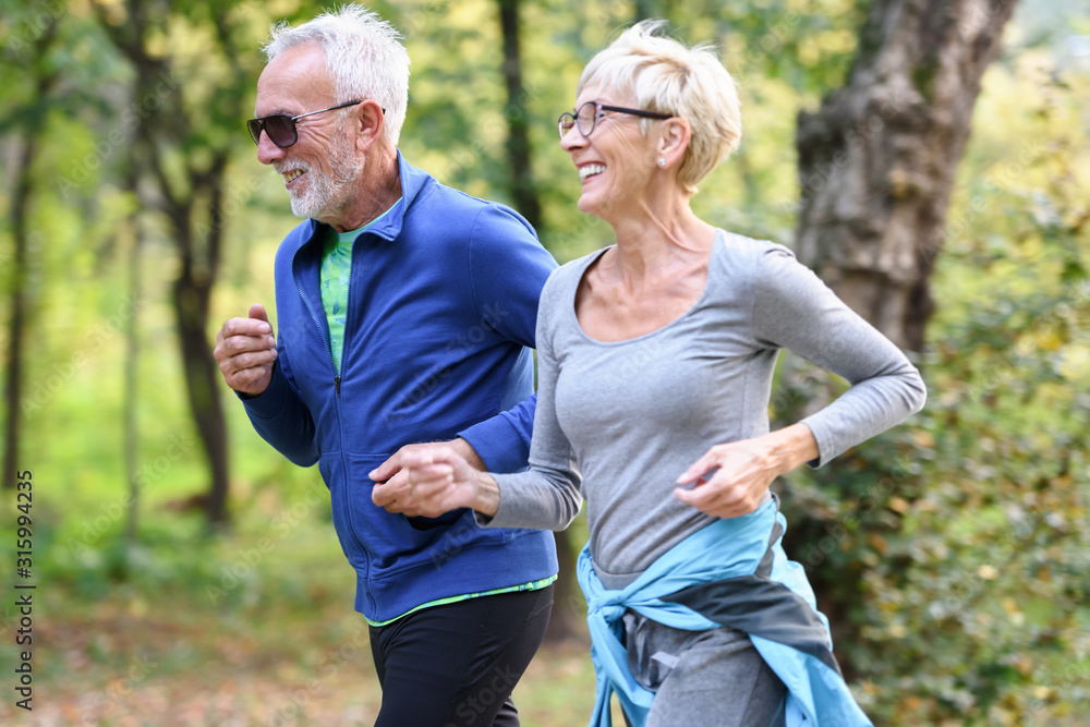 Cheerful active senior couple jogging in the park. Exercise together to stop aging.