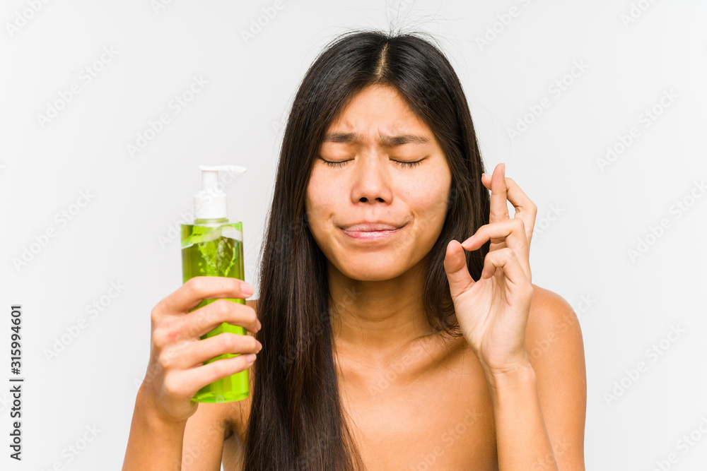 Young chinese woman holding a moisturizer with aloe vera isolated crossing fingers for having luck Young chinese woman holding a moisturizer with aloe vera isolated crossing fingers for having luck