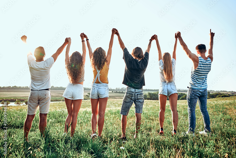 Obraz premium Group of happy young people holding hands raised together on the sky background