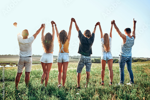 Group of happy young people holding hands raised together on the sky background