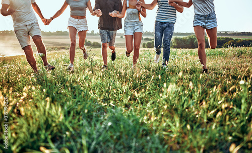 Group of friends running on grass meadow on country side.