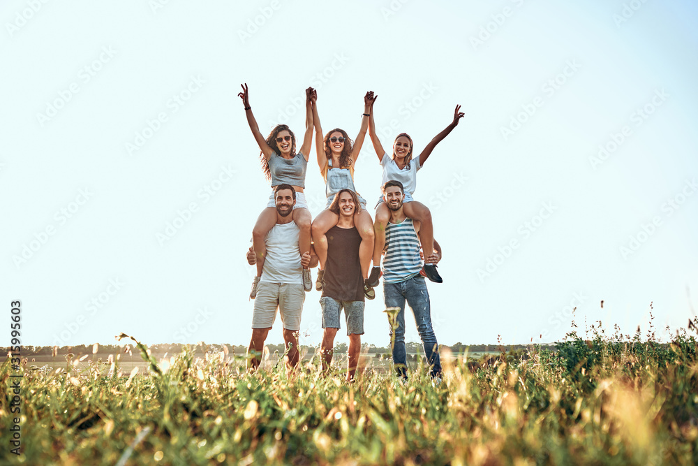 Attractive women dancing to music while sitting on shoulders of boyfriends at outdoor party Attractive women dancing to music while sitting on shoulders of boyfriends at outdoor party