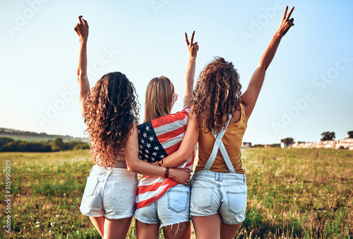 Fotografie Three happy young women with national american flag on a field