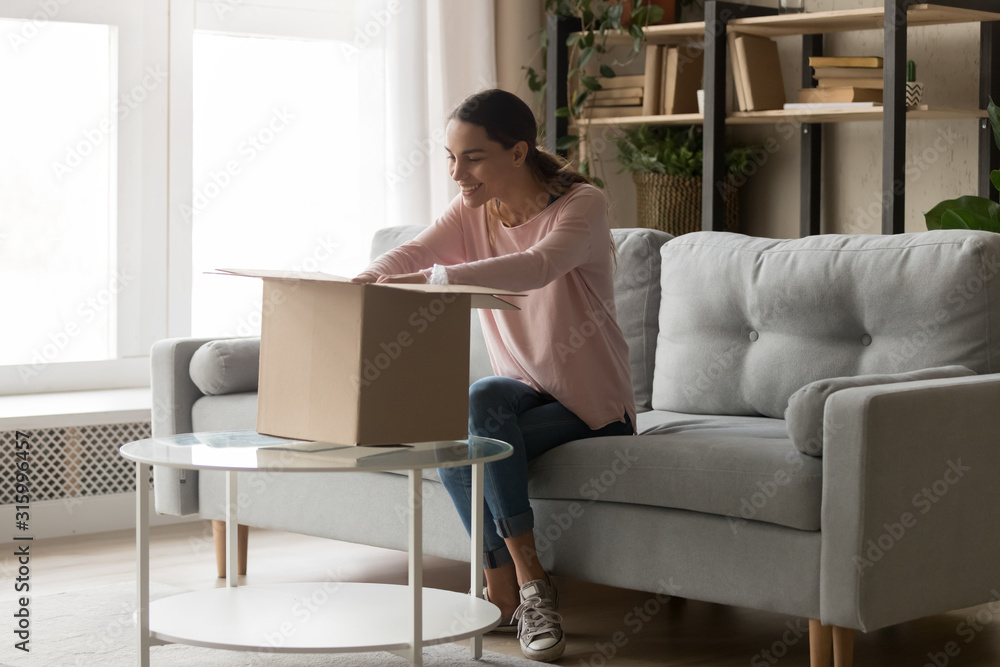 Happy millennial girl unpacking huge cardboard parcel at home. Happy millennial girl unpacking huge cardboard parcel at home.