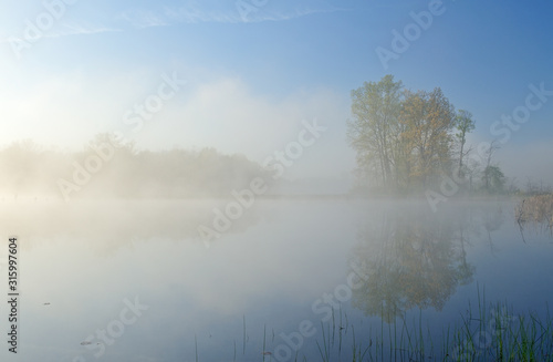 Spring landscape at sunrise of foggy Jackson Hole Lake with reflections in calm water, Fort Custer State Park, Michigan