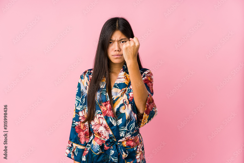 Young asian woman wearing a kimono pajamas showing fist to camera, aggressive facial expression. Young asian woman wearing a kimono pajamas showing fist to camera, aggressive facial expression.