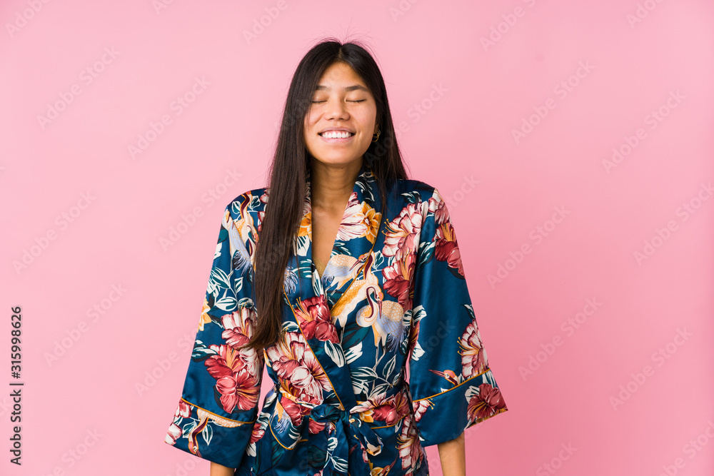 Young asian woman wearing a kimono pajamas laughs and closes eyes, feels relaxed and happy. Young asian woman wearing a kimono pajamas laughs and closes eyes, feels relaxed and happy.