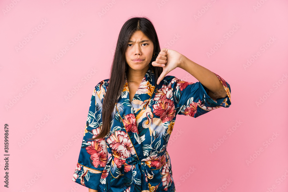 Young asian woman wearing a kimono pajamas showing a dislike gesture, thumbs down. Disagreement concept. Young asian woman wearing a kimono pajamas showing a dislike gesture, thumbs down. Disagreement concept.