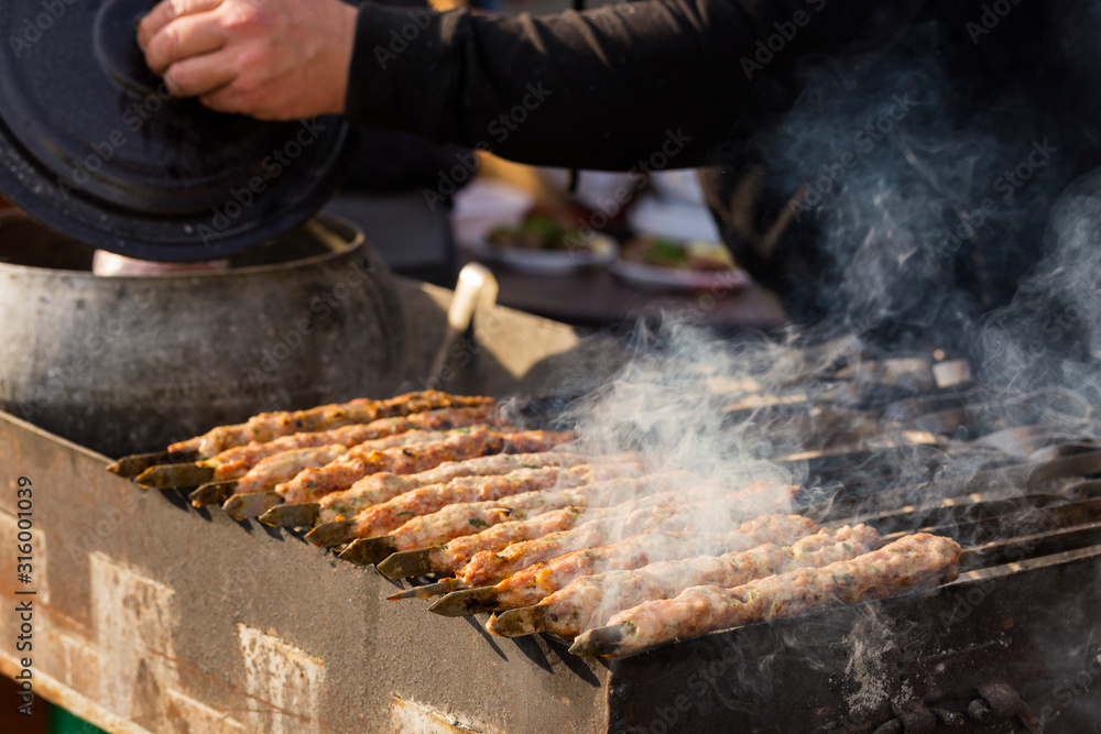 Meat slices prepare on fire. Baked meat on skewers. A cook is preparing a hot meal outdoors. Hands of the master.