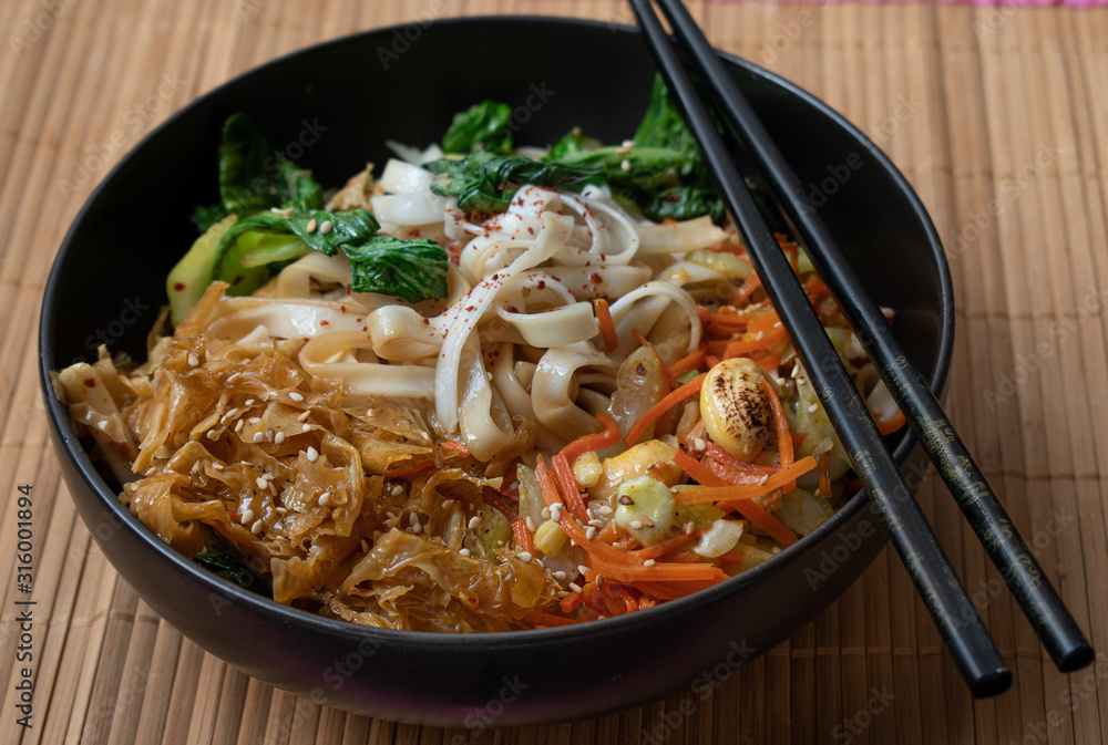 Vegan stir fry consisting of yuba, carrot, bok choy and noodles, served in black bowl Vegan stir fry consisting of yuba, carrot, bok choy and noodles, served in black bowl