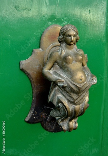 Bronze naked woman door handle on green door.