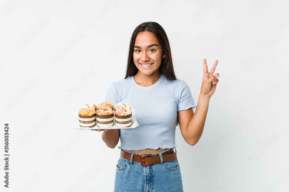 Young mixed race indian holding a sweet cakes showing number two with fingers. Young mixed race indian holding a sweet cakes showing number two with fingers.
