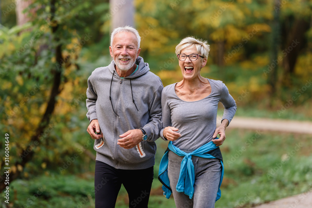 Cheerful active senior couple jogging in the park. Exercise together to stop aging. - obrazy, fototapety, plakaty 