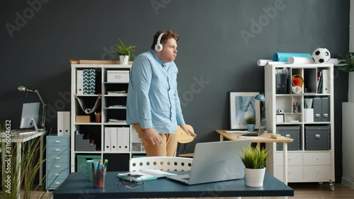 Slow motion of funny employee attractive guy dancing in office room wearing headphones having fun alone. Modern gadgets, joy and entertainment concept. photo
