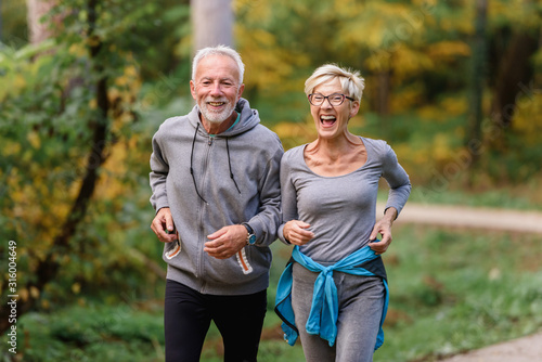 Tablou canvas Cheerful active senior couple jogging in the park