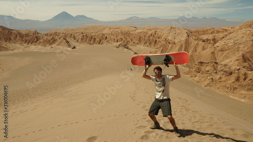 Man with sand board at a dune in the Atacama desert near San Pedro de Atacama, Chile.