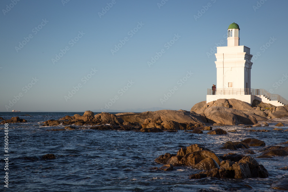 St Helena Bay, Cape Town, South Africa - August 26 2017: White Light House on the beach with ocean and rocks in the foreground in St Helena Bay West Coast Cape Town South Africa