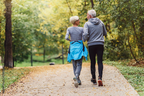 Cheerful active senior couple jogging in the park. Exercise together to stop aging. photo