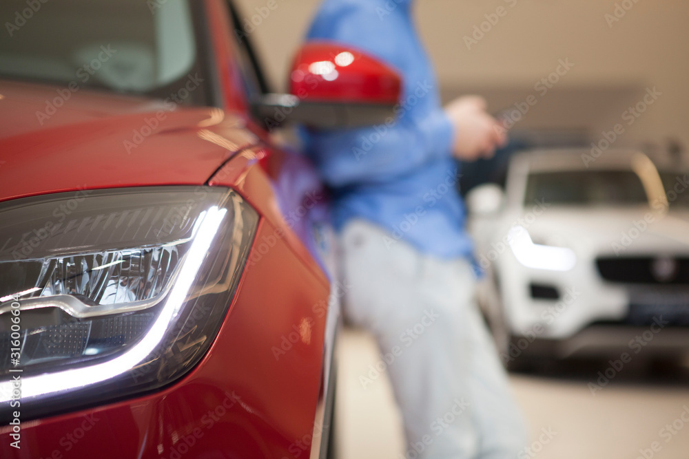 Cropped close up shot of car lights, unrecognizable man leaning on the car on blurred background