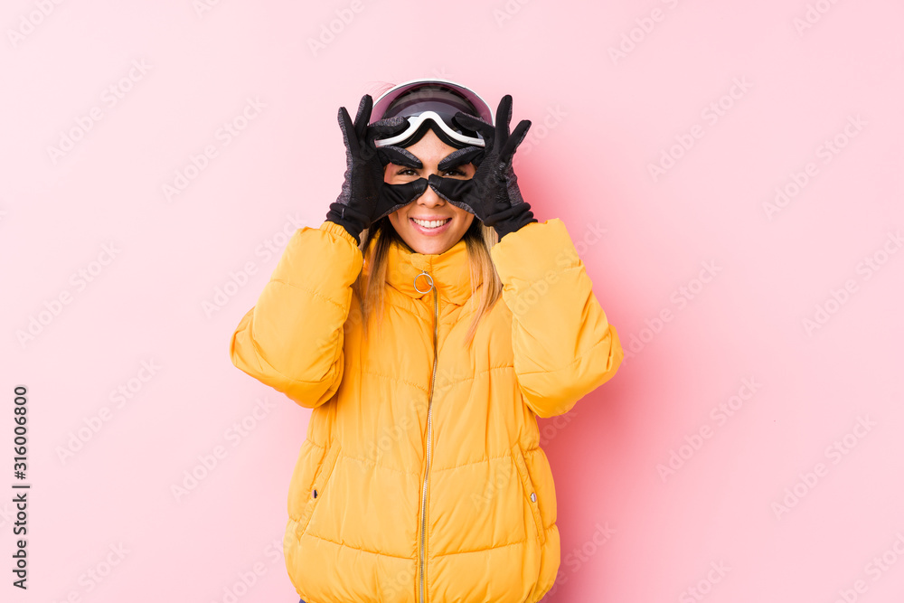 Young caucasian woman wearing a ski clothes in a pink background showing okay sign over eyes Young caucasian woman wearing a ski clothes in a pink background showing okay sign over eyes